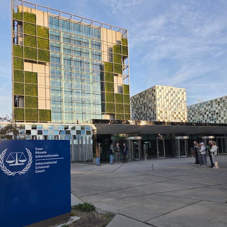 Het gebouw van het Internationaal Strafhof in Den Haag, met op de voorgrond het bord van de Cour P&eacute;nale Internationale en bij de ingang groepjes deelnemers met irissen